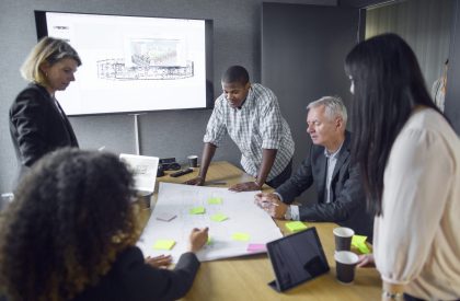A diverse team collaborates on a project around a conference table with notes and designs.
